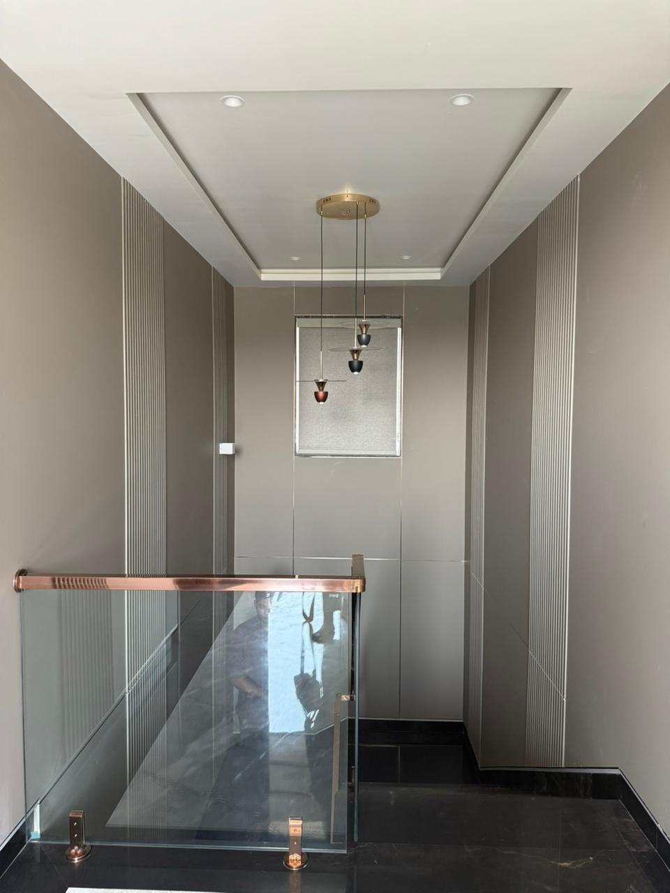 Staircase landing with rose-gold glass railing, fluted wall panelling, and pendant lighting